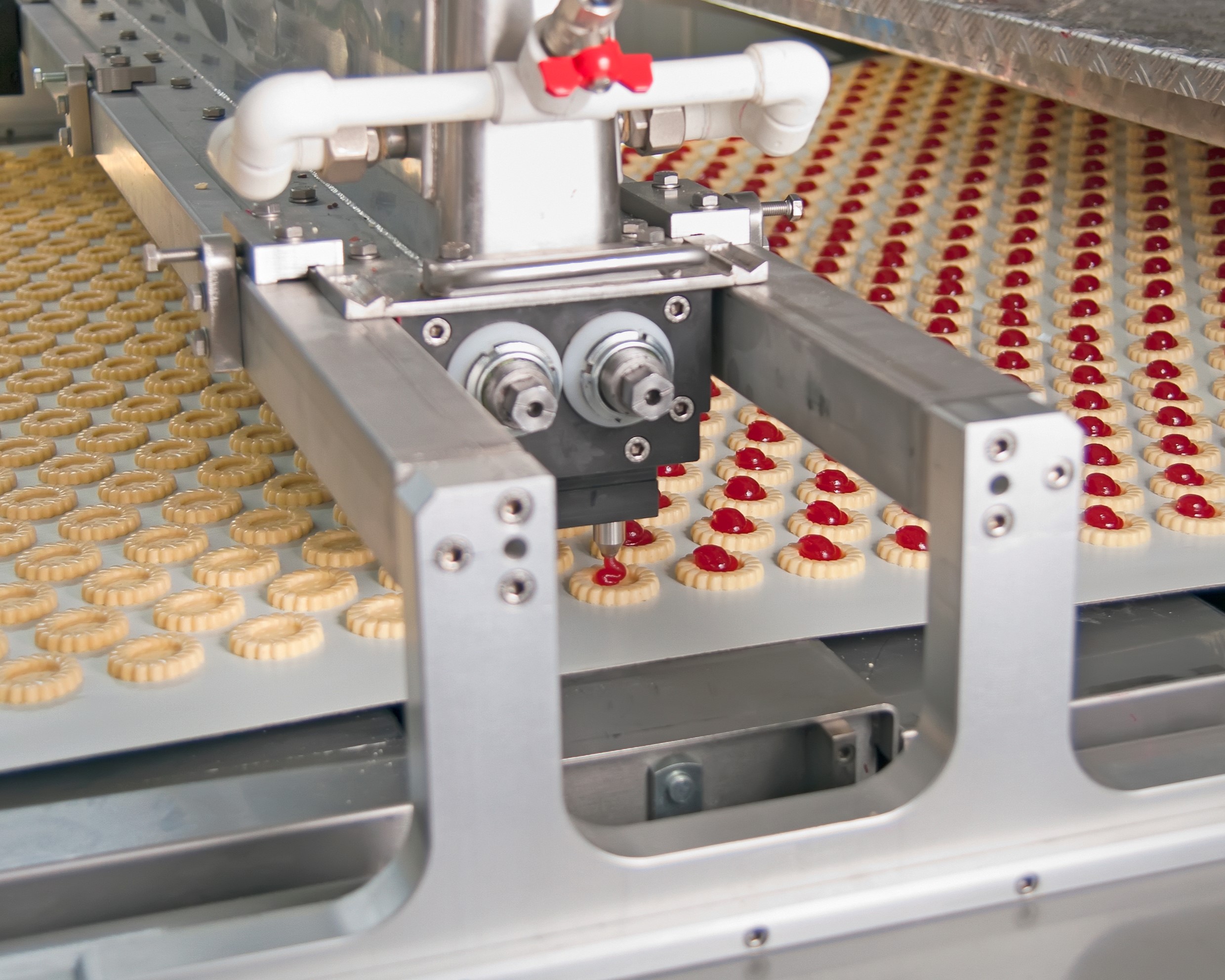 Automated machine pumping jam onto biscuits.